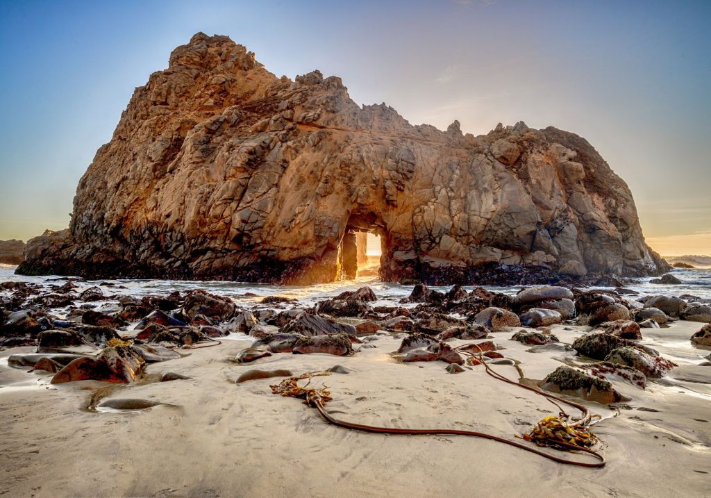 large rock formation with sun coming through at the beach 